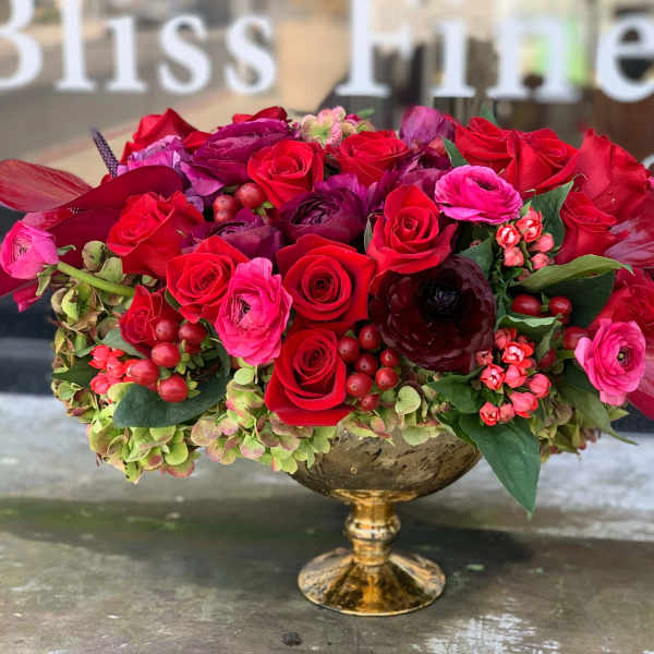 Red and pink rose arrangement in a gold pedestal vase