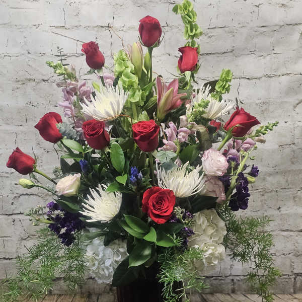 Tall vase arrangement with red roses, white spider mums, and mixed blooms