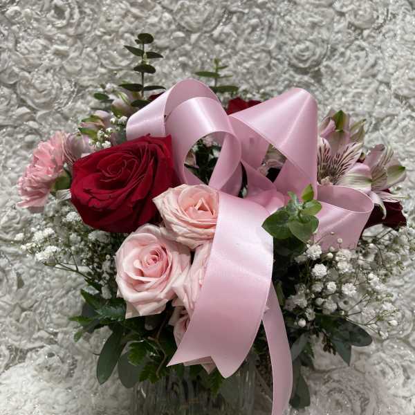 Pink and red roses in a glass vase with a pink ribbon