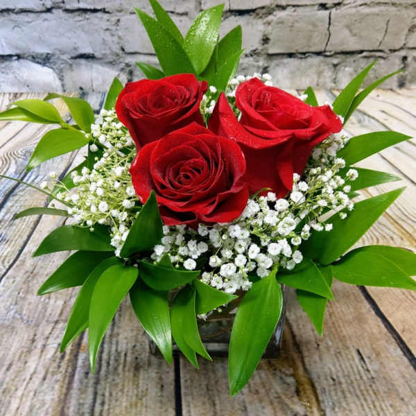 Three red roses in a low glass vase with white filler flowers