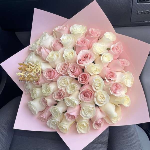 Bouquet of pink and ivory roses wrapped in pink paper with a small decorative crown accent