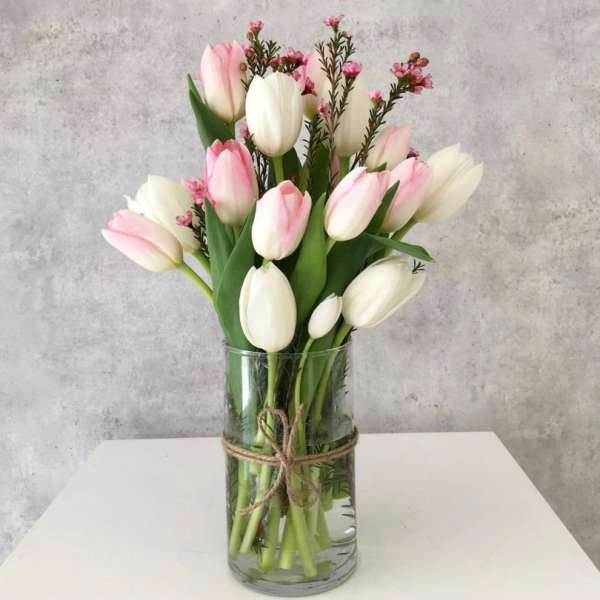 Pink and white tulips in a clear glass vase tied with twine