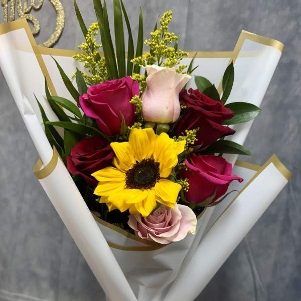 Bouquet of roses and a sunflower wrapped in white paper with a gold ribbon