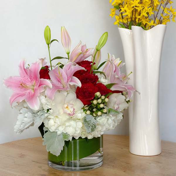 Pink lilies and red roses in a glass vase with white hydrangeas