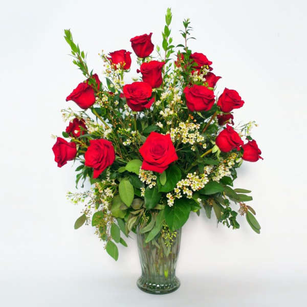Red roses arranged in a clear glass vase with small white filler flowers