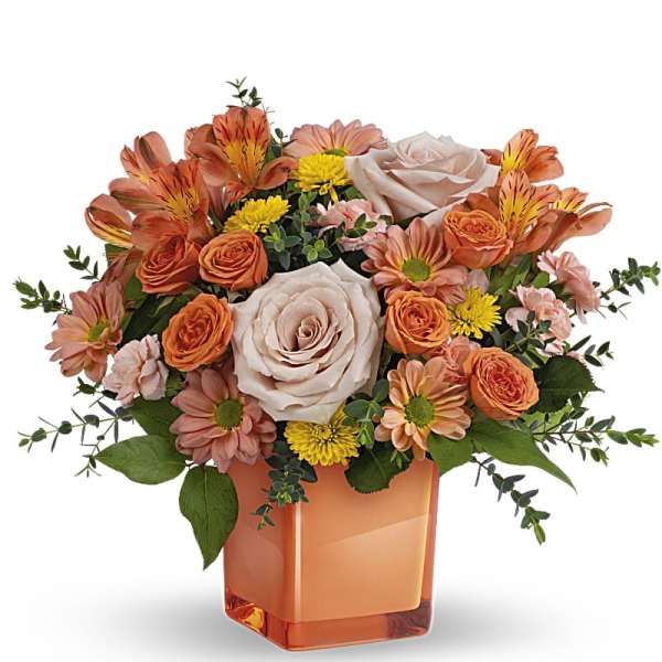 Orange and blush bouquet in a square glass vase