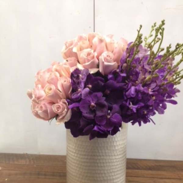 Pink roses and purple orchids arranged in a white vase