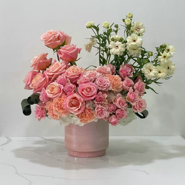 Pink roses and peach carnations in a pink vase with white flowers