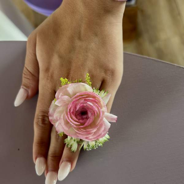 Pink ranunculus wrist corsage on a hand