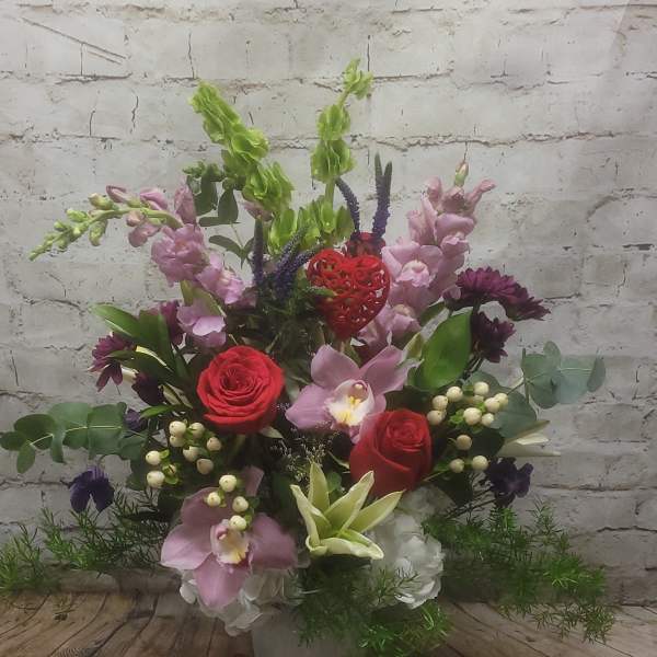 Mixed floral arrangement in a gray vase with red roses and pink orchids