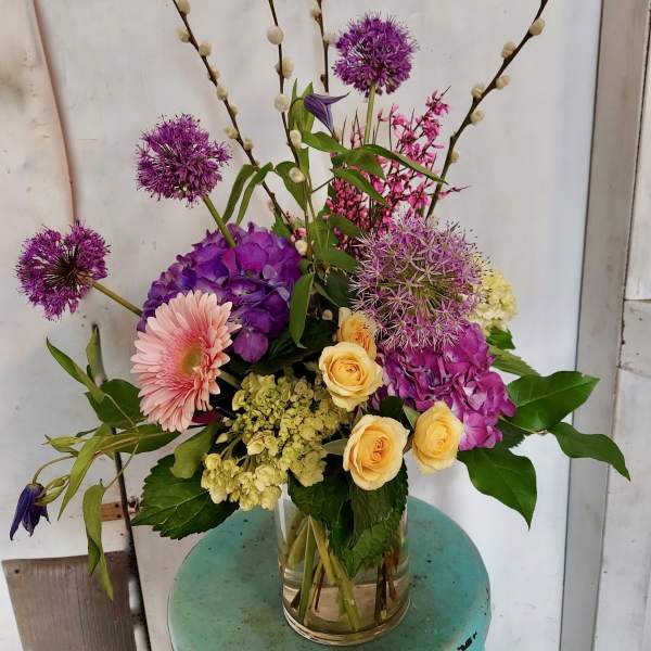 Mixed bouquet of purple, pink, and yellow flowers in a clear glass vase