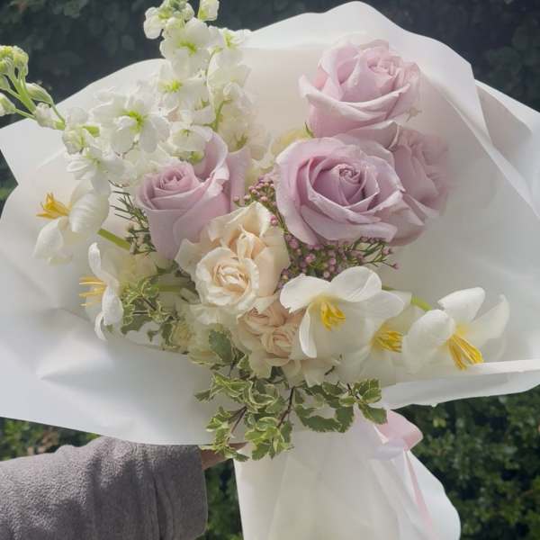 Handheld bouquet of pale pink and white flowers wrapped in white paper