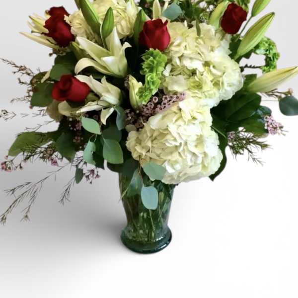 Red roses and white lilies with hydrangeas in a green glass vase