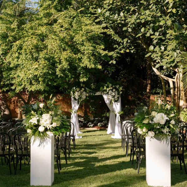 Outdoor wedding aisle with white floral arrangements and a draped arch