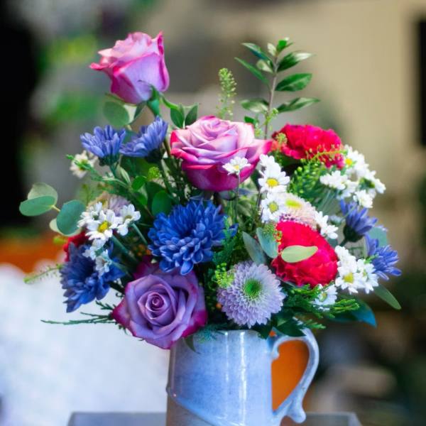 Mixed bouquet of roses and daisies in a blue ceramic mug