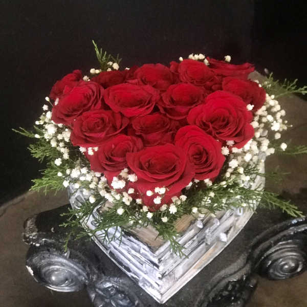 Heart-shaped bouquet of red roses with white baby's breath in a clear vase