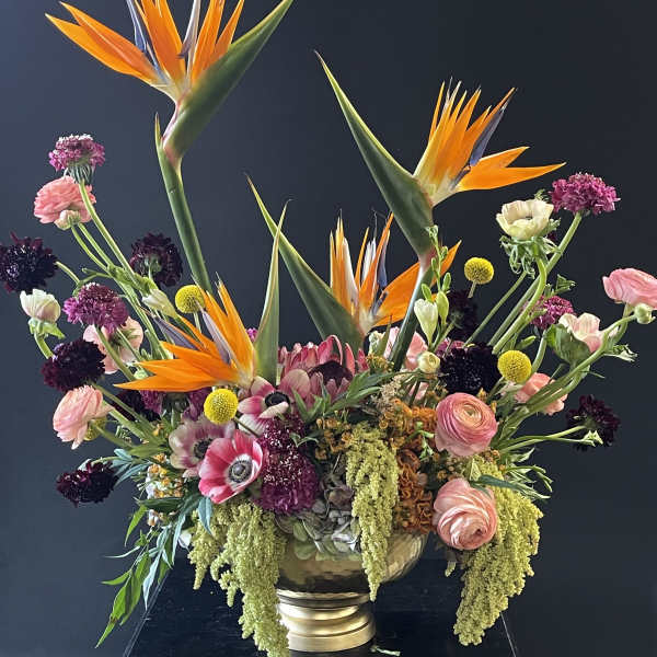 Large mixed floral arrangement with orange bird-of-paradise and pink blooms in a gold vase