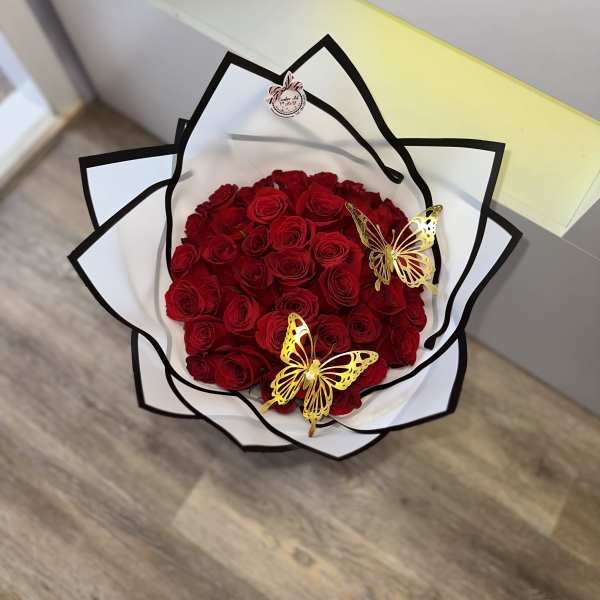Bouquet of red roses wrapped in white paper with black trim and gold butterfly accents