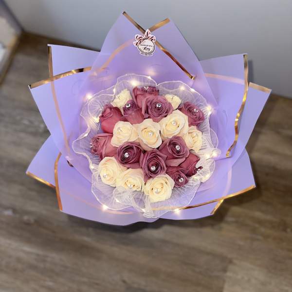 Bouquet of pink and cream roses wrapped in lavender paper