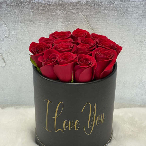 Black hatbox of red roses with gold 'I Love You' text, displayed on white fur.