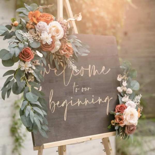 Floral welcome sign on an easel with roses and greenery