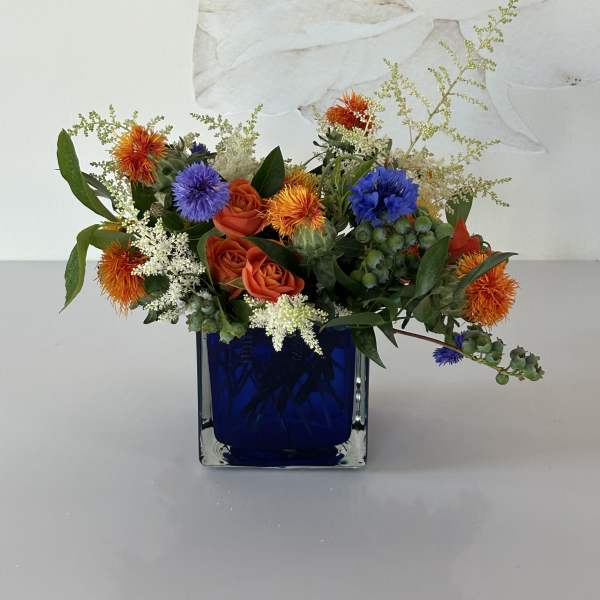 Mixed bouquet of orange and blue flowers in a cobalt glass vase