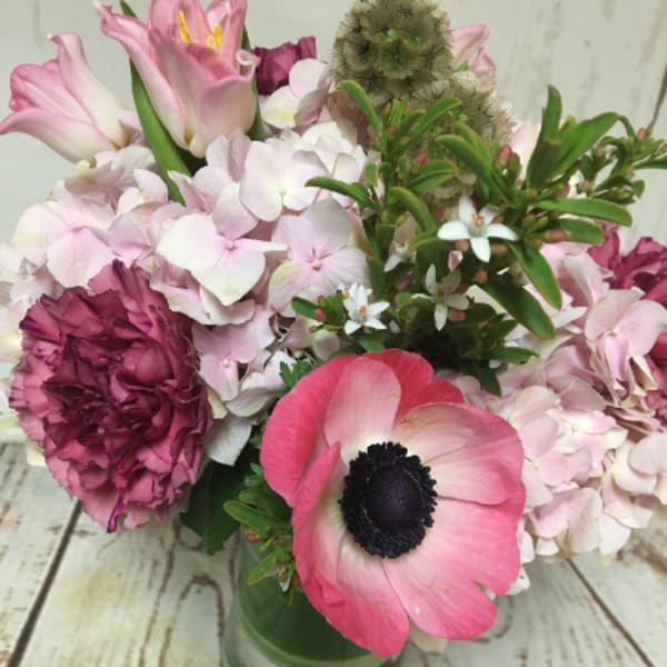 Compact pink and white mixed flower arrangement in a clear glass vase on a rustic wood surface