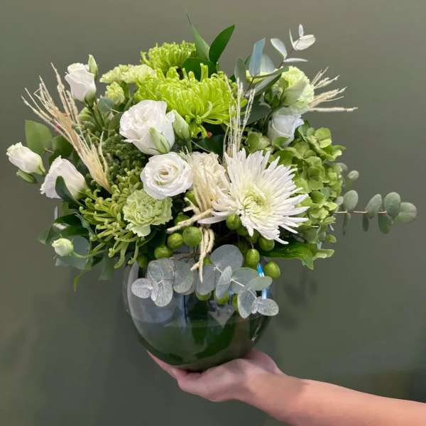 Green and white floral arrangement in a dark glass vase