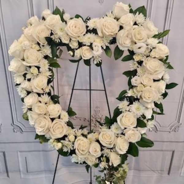 Heart-shaped white floral wreath on a black stand
