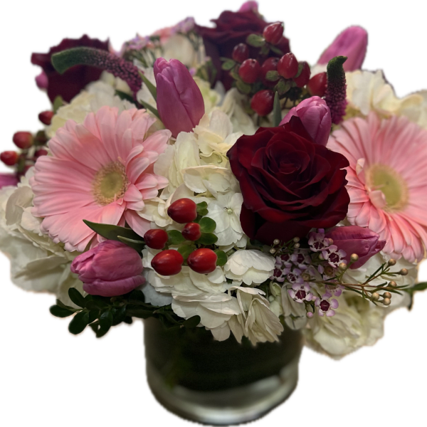 Bouquet of pink gerbera daisies, red roses, and white hydrangeas in a glass vase
