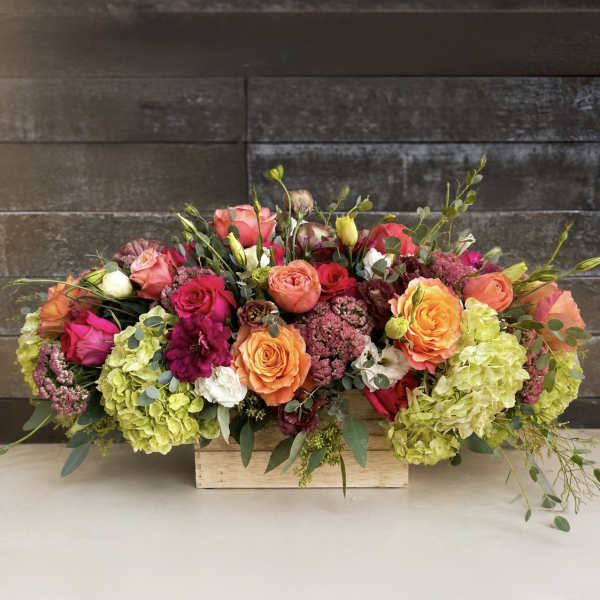 Low floral arrangement in a wooden box with roses and hydrangeas