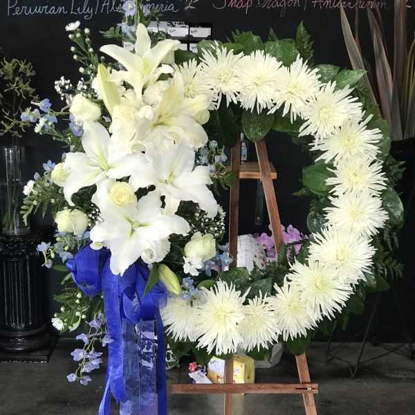 White floral funeral wreath on an easel with a blue ribbon