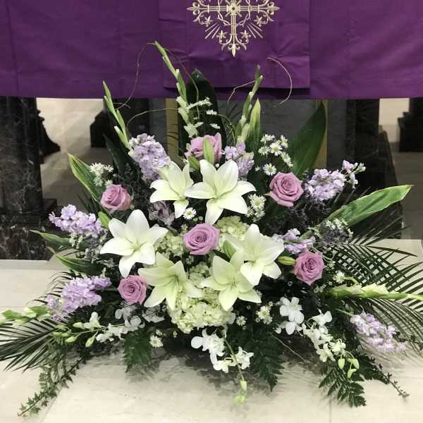 Symmetrical funeral arrangement with white lilies, lavender roses, and purple flowers