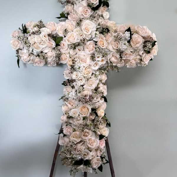 Cross-shaped floral arrangement of pale roses and white blooms on a stand