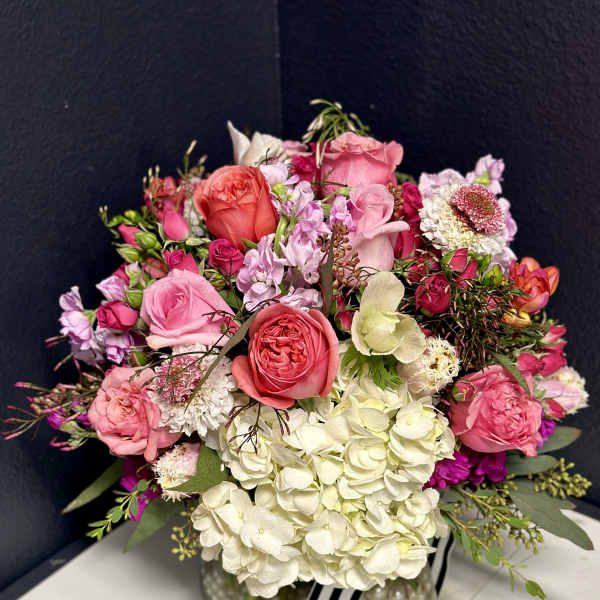 Pink and white rose bouquet in a clear glass vase with a striped ribbon
