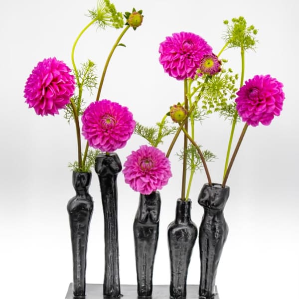 Five magenta flowers arranged in black sculptural vases on a rectangular base.