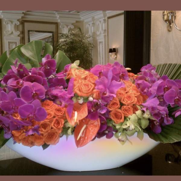 Large arrangement of purple orchids and orange roses in a white bowl vase