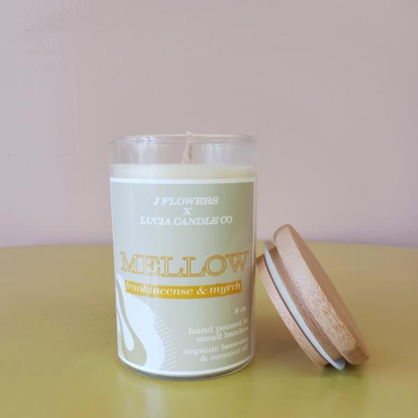 A scented candle in a glass jar with a wooden lid beside it