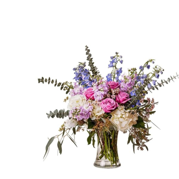Bouquet of pink roses, blue delphinium, and white hydrangeas in a glass vase