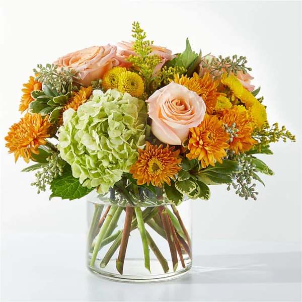 Bouquet of peach roses, green hydrangea, and orange mums in a glass vase