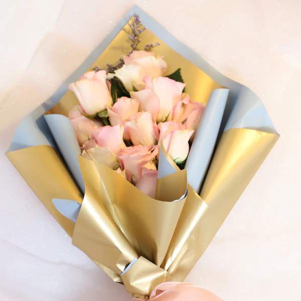 Bouquet of pale pink roses wrapped in blue and gold paper with a pink ribbon