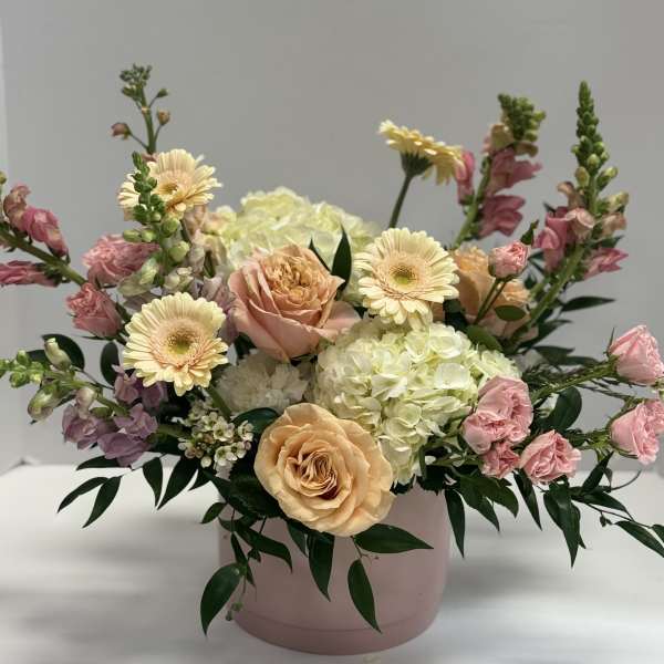 Pastel floral arrangement in a pink round box with roses, gerberas, and hydrangea