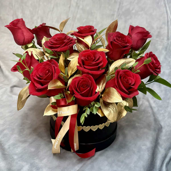 Red roses arranged in a black round box with gold leaves and ribbon