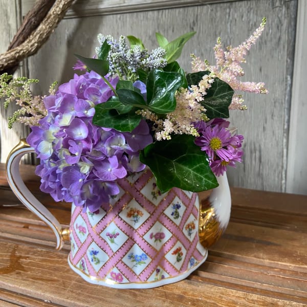 Purple hydrangea and daisy bouquet in a patterned teacup vase