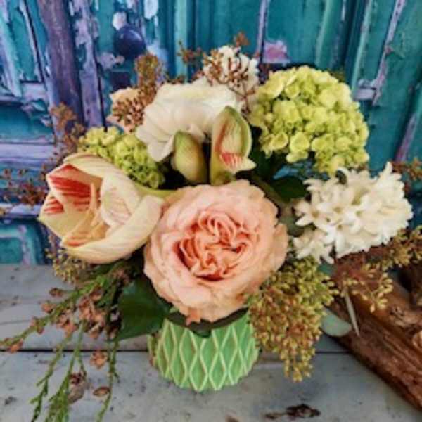 Bouquet of peach roses, white amaryllis, and pale green hydrangeas in a green vase