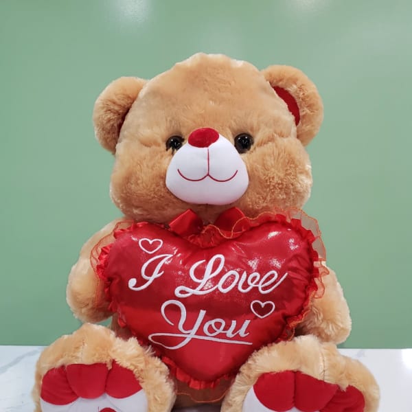 Plush teddy bear holding a red heart pillow that says "I Love You"
