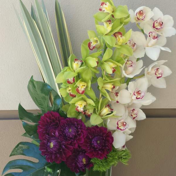 Orchid and purple chrysanthemum arrangement in a tall glass vase