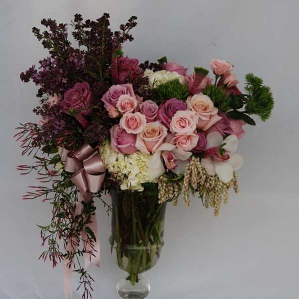 Pink and white rose bouquet in a clear glass vase with a ribbon