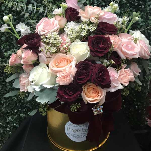 Bouquet of pink, burgundy, and white roses in a gold hatbox with ribbon