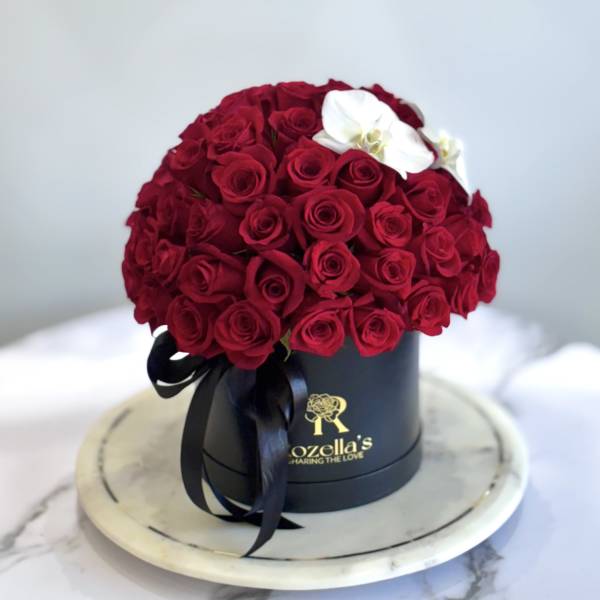 Red rose arrangement in a black hatbox with a white orchid accent